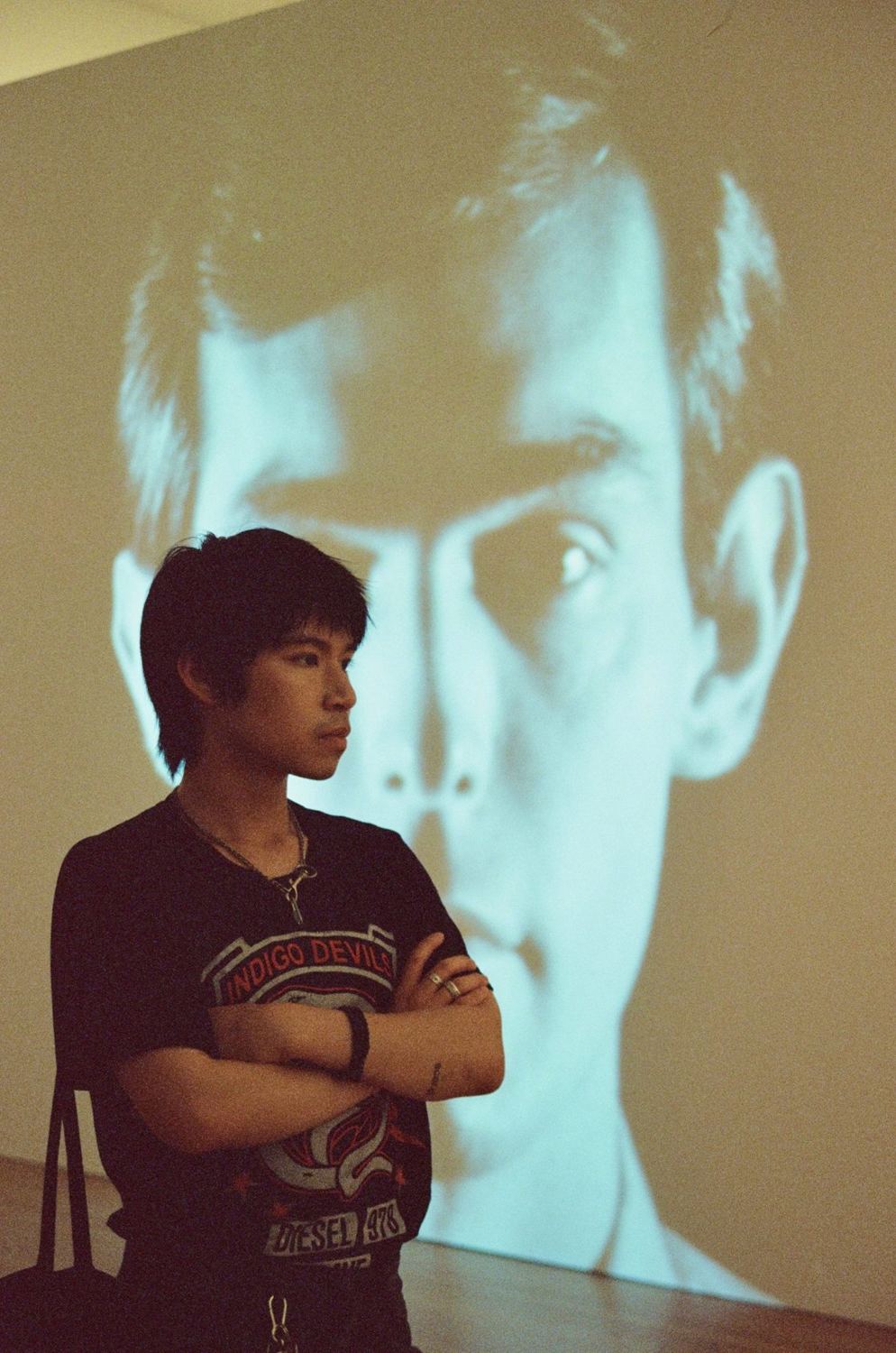 A person with arms crossed in front of a large projected face